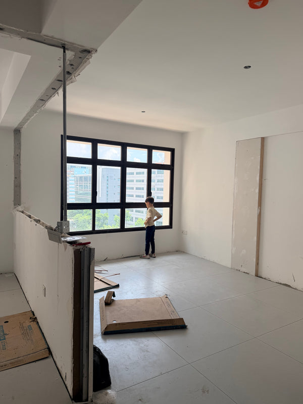 child standing in a room with large windows and construction materials on the floor after hacking walls, tiling floor, ew drywall in singapore bto renovation project.