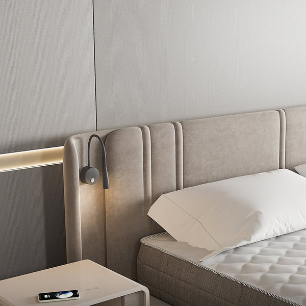 Beige upholstered bed with white pillows and a nightstand featuring a phone, against a neutral wall.