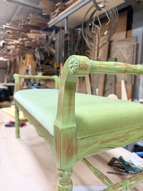 A painted wooden bench with a distressed sage green finish, featuring a cushioned seat, shown in HomeShake's workshop in Singapore.