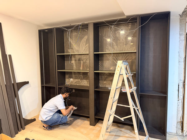 singaporean carpenter installing a display cabinet and shelves in a showroom with a ladder